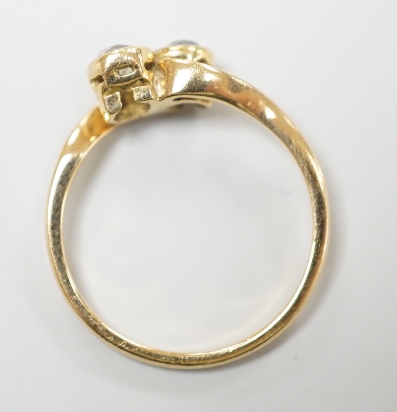 A yellow metal and collet set two stone diamond cross over ring, size L, gross weight 1.9 grams.